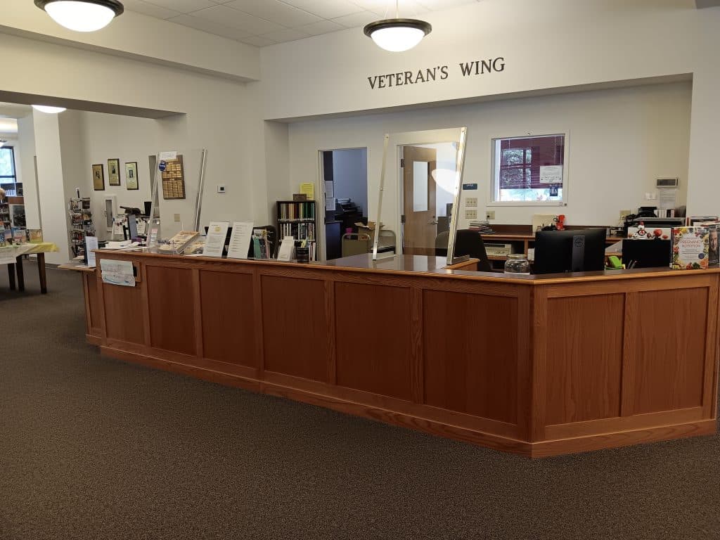 The library's main circulation desk. There are 2 workstations and above the desk there are letters on the wall that read "Veteran's Wing"
