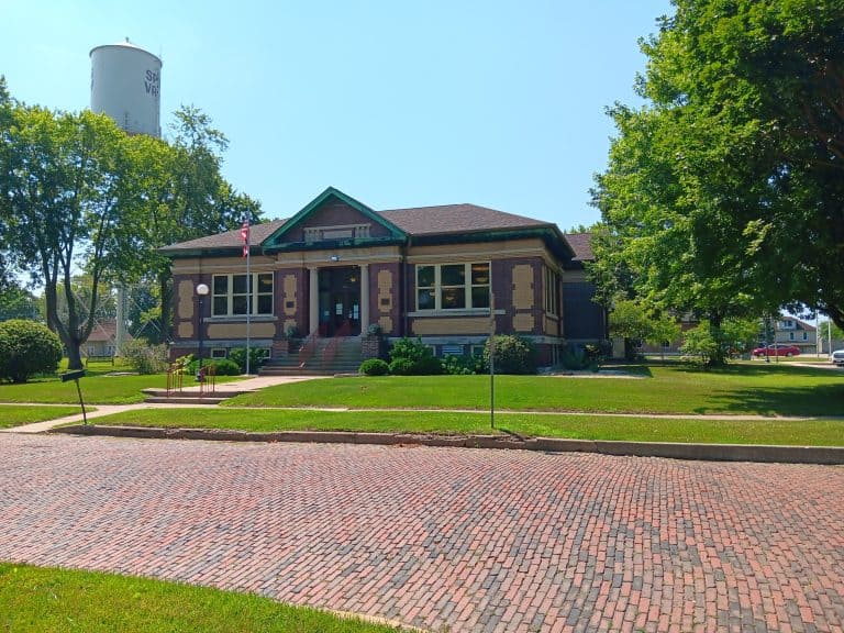 Side entrance of Richard A. Mautino Memorial library. A Carnegie building with an American flag by the side door and Spring Valley's water tower behind.